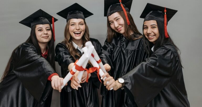 A joyful group of multiracial women in graduation gowns holding diplomas.